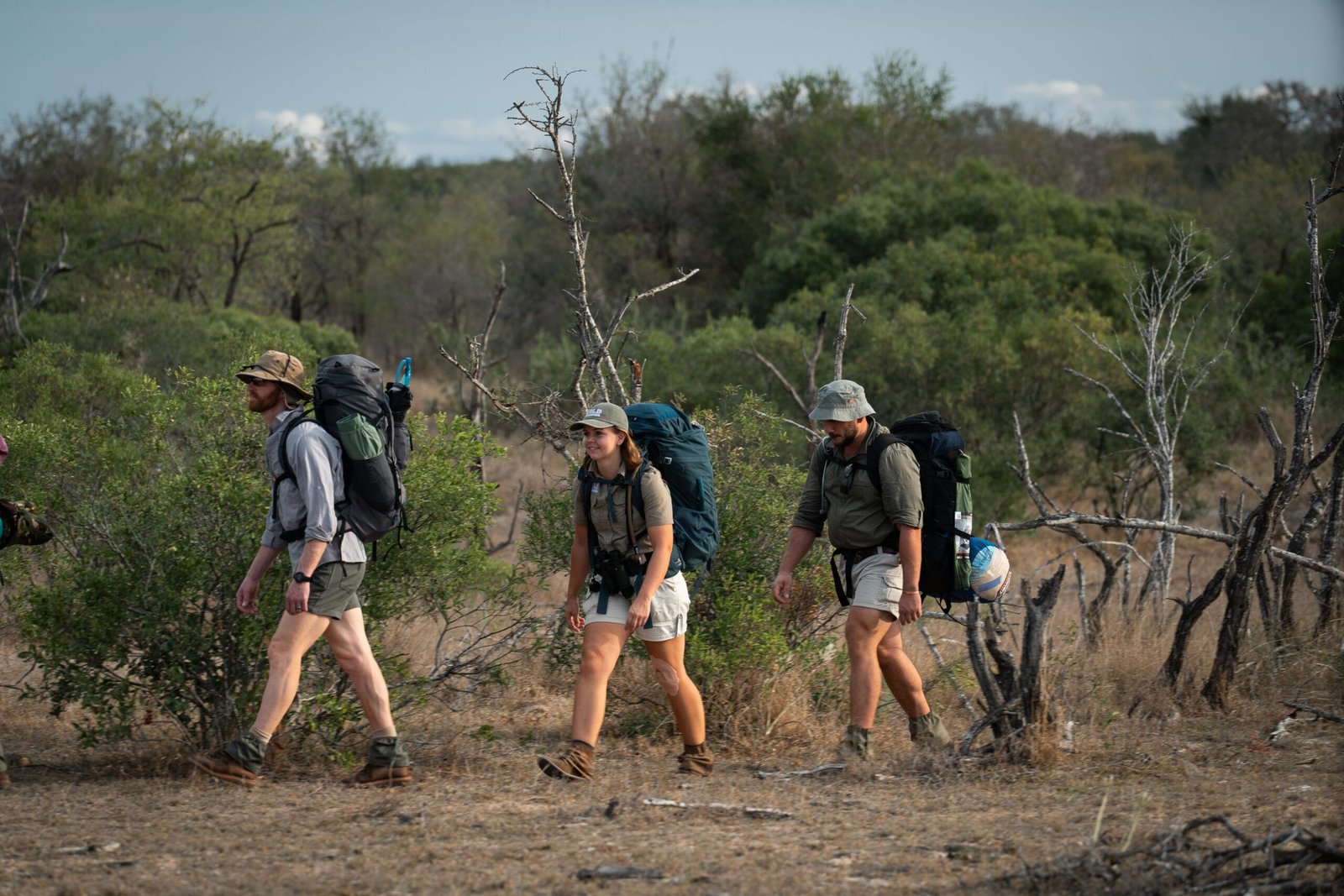 Daphne wandelt met twee deelnemers en hun backpacks door de Afrikaanse wildernis tijdens de Primitive Trail in Greater Kruger, gefotografeerd vanaf de zijkant.