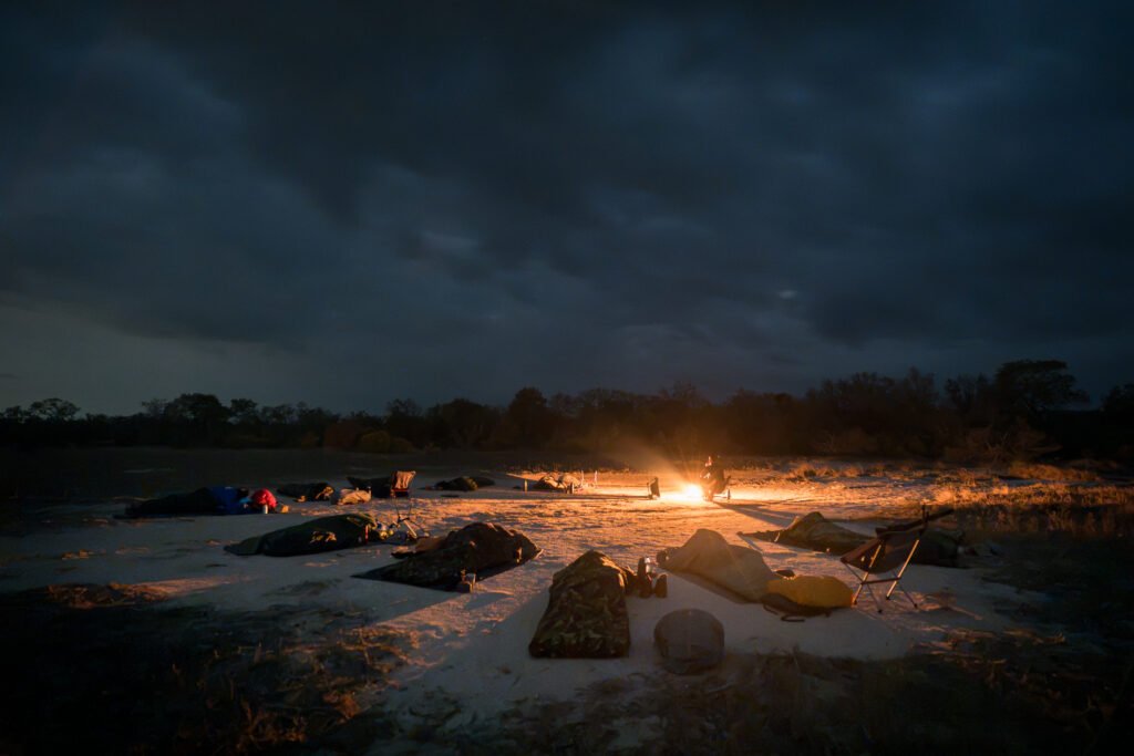 Een deelnemer houdt 's nachts de wacht bij het kampvuur terwijl de rest van de groep slaapt in het bushkamp tijdens de Primitive Trail in Greater Kruger.
